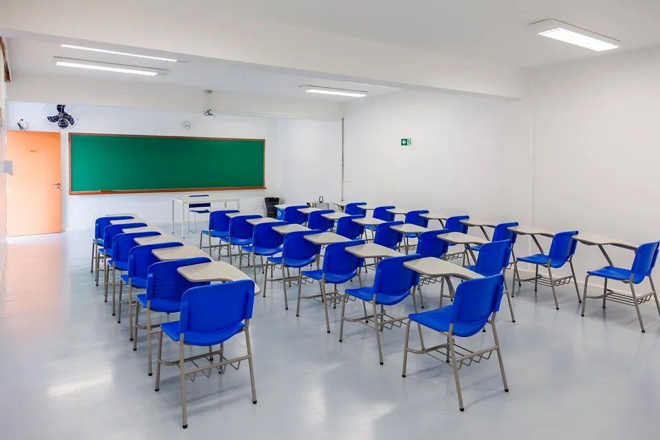 Uma sala de aula com cadeiras e mesas azuis e um quadro verde.