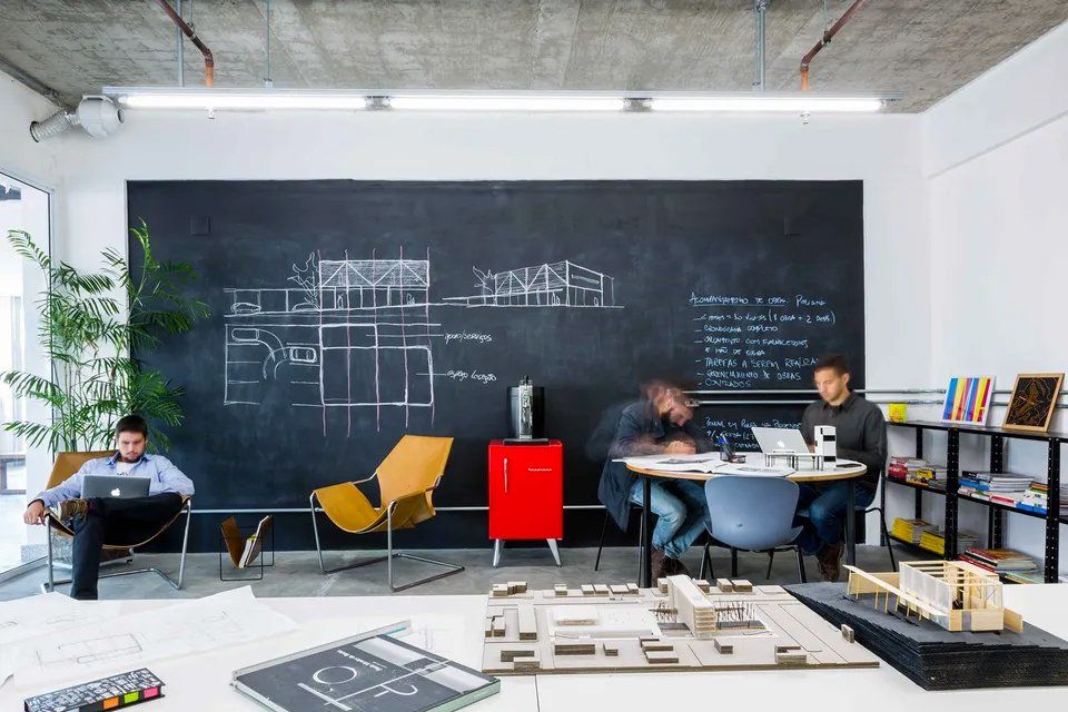 Dois homens estão sentados a uma mesa em frente a um quadro negro.