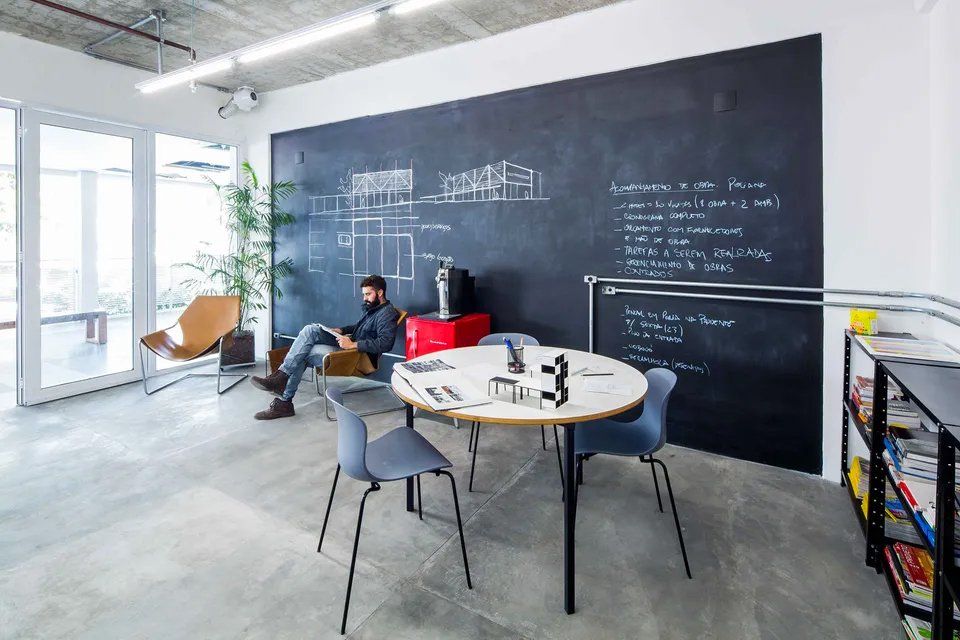 Um homem está sentado a uma mesa em frente a um quadro negro em uma sala.