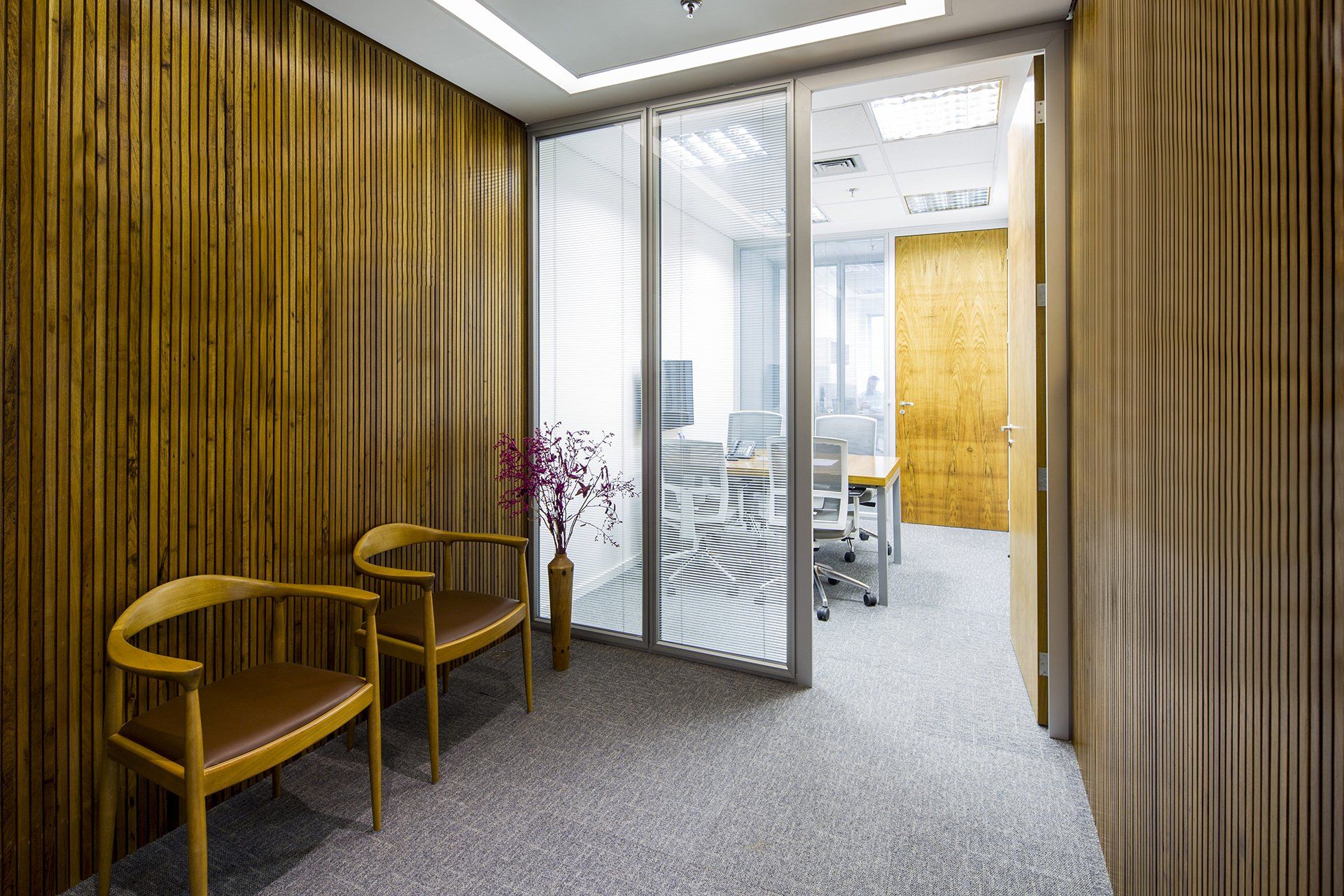 Uma sala de espera com duas cadeiras e uma porta de vidro que dá acesso a uma sala de conferências.