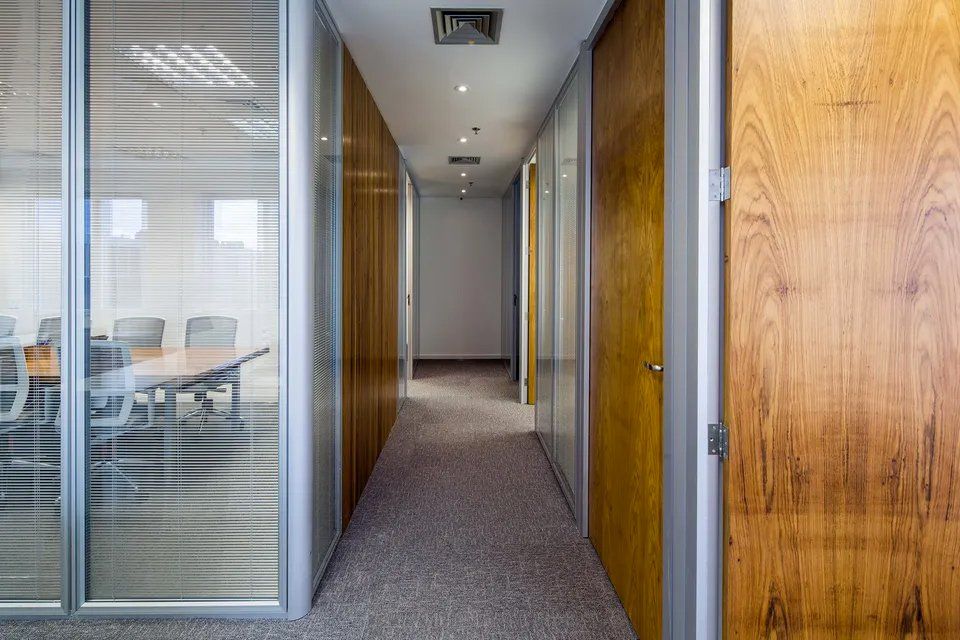 Um longo corredor em um prédio de escritórios com uma porta de madeira e uma parede de vidro.
