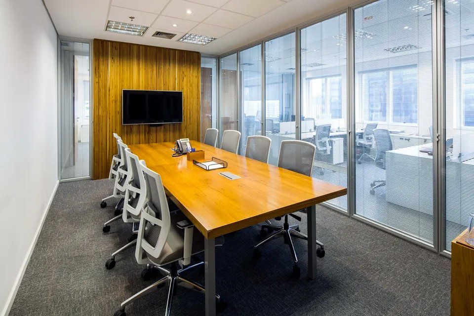 Uma sala de conferências com uma longa mesa e cadeiras de madeira e uma TV de tela plana.