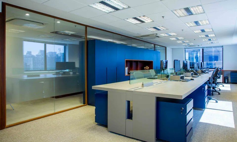 Um amplo escritório com móveis azuis e brancos e parede de vidro.