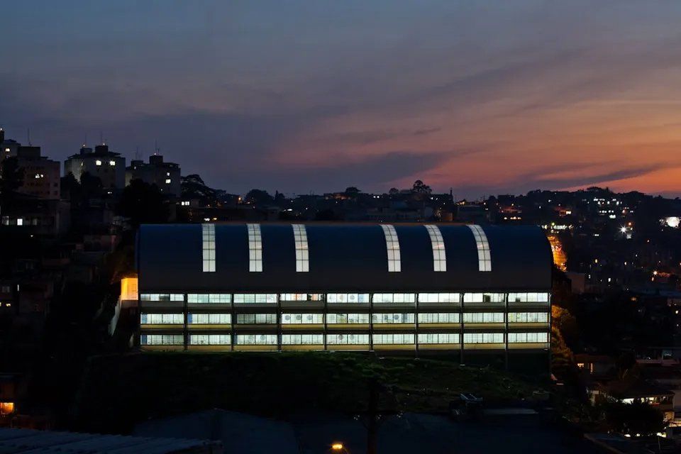 Um grande edifício é iluminado à noite com uma cidade ao fundo