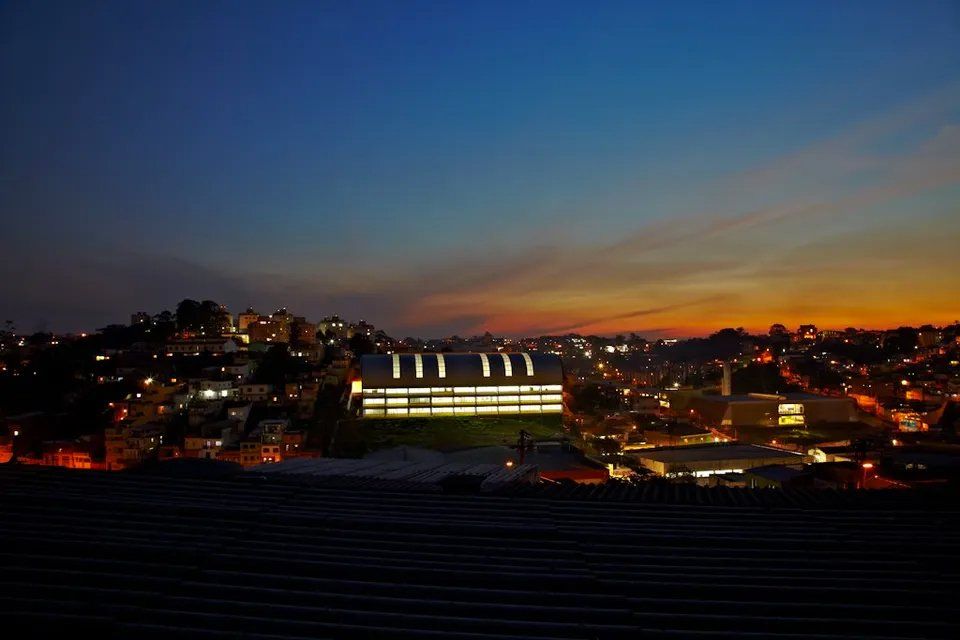Uma cidade à noite com um prédio em primeiro plano e um pôr do sol ao fundo.