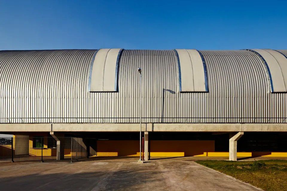 Um grande edifício com telhado curvo e um céu azul ao fundo.