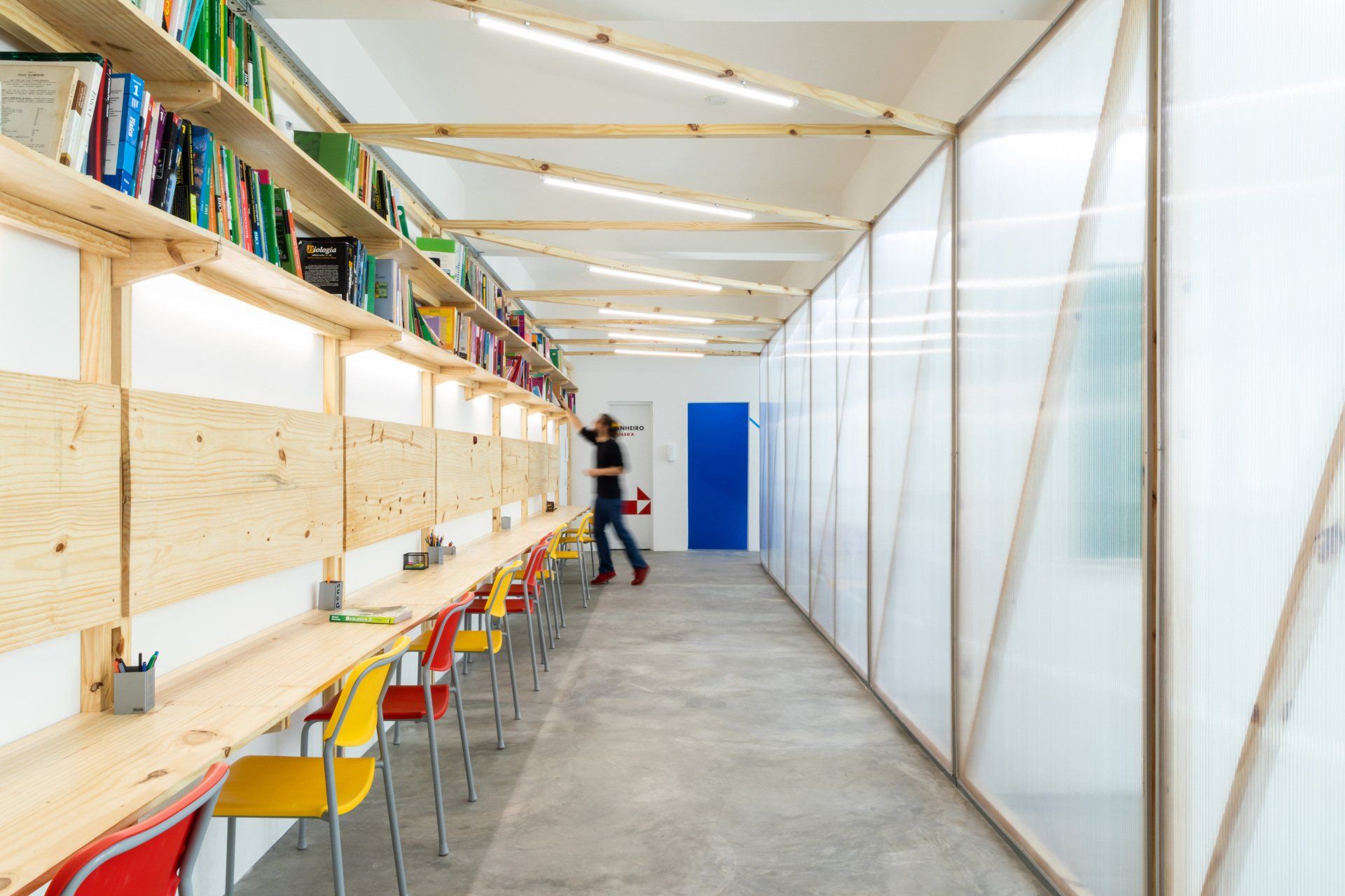 Uma mulher está andando por um corredor cheio de mesas e cadeiras.