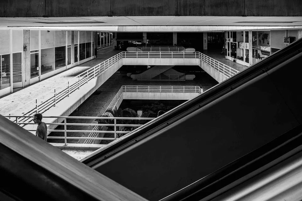 Uma foto em preto e branco de uma escada rolante em um prédio.