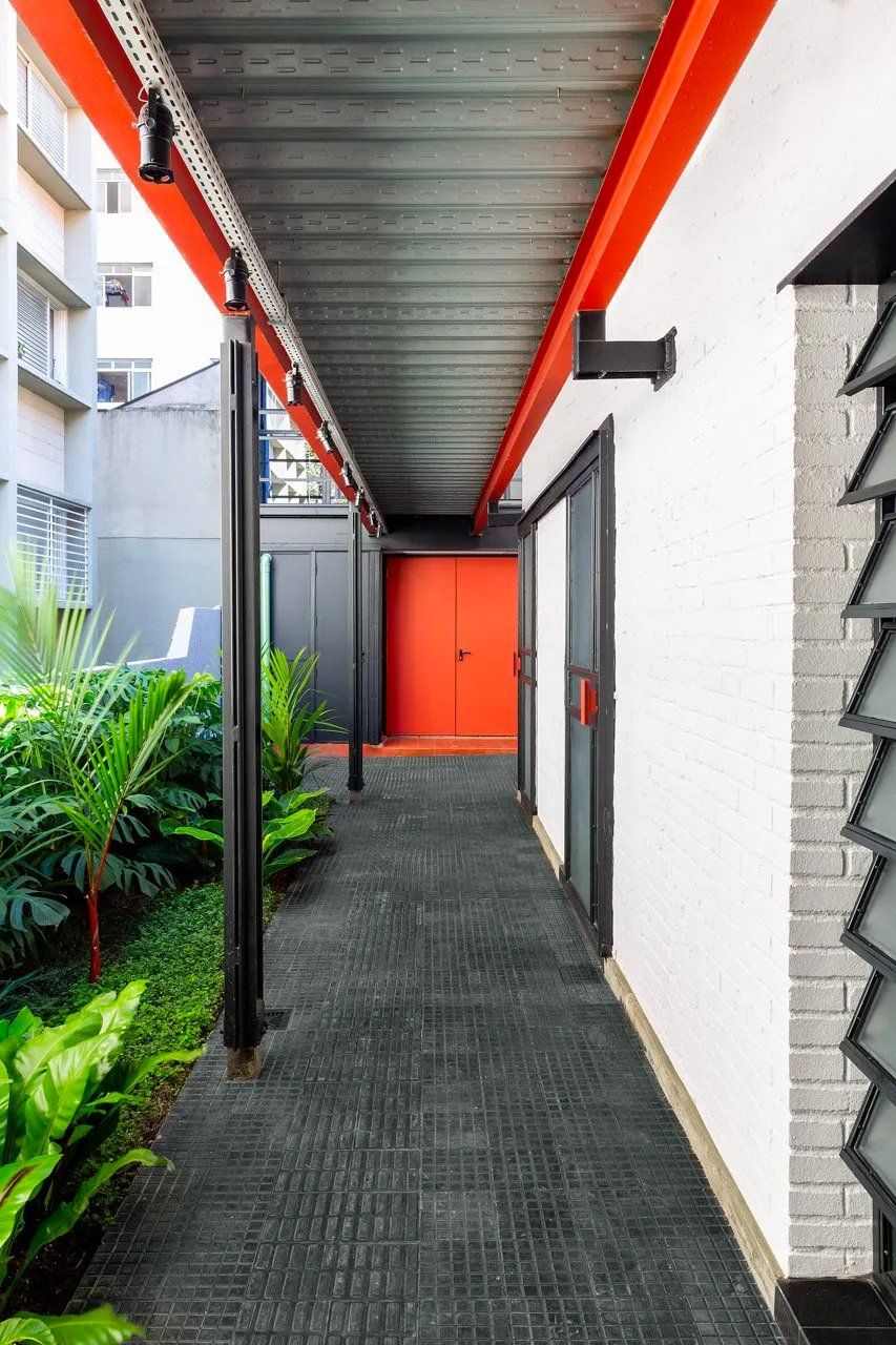 Um longo corredor entre dois edifícios com uma porta vermelha.