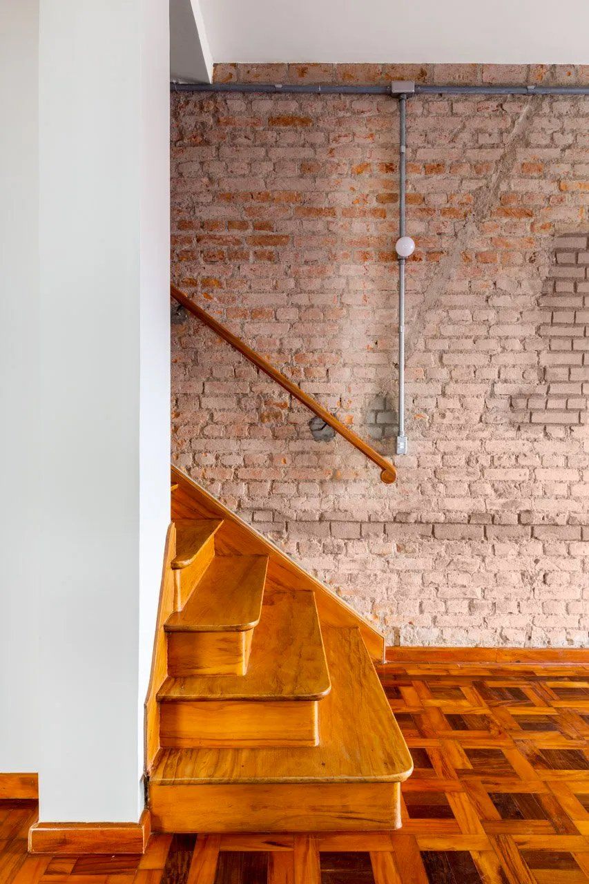 Uma escada de madeira que leva até uma parede de tijolos com corrimão de madeira.