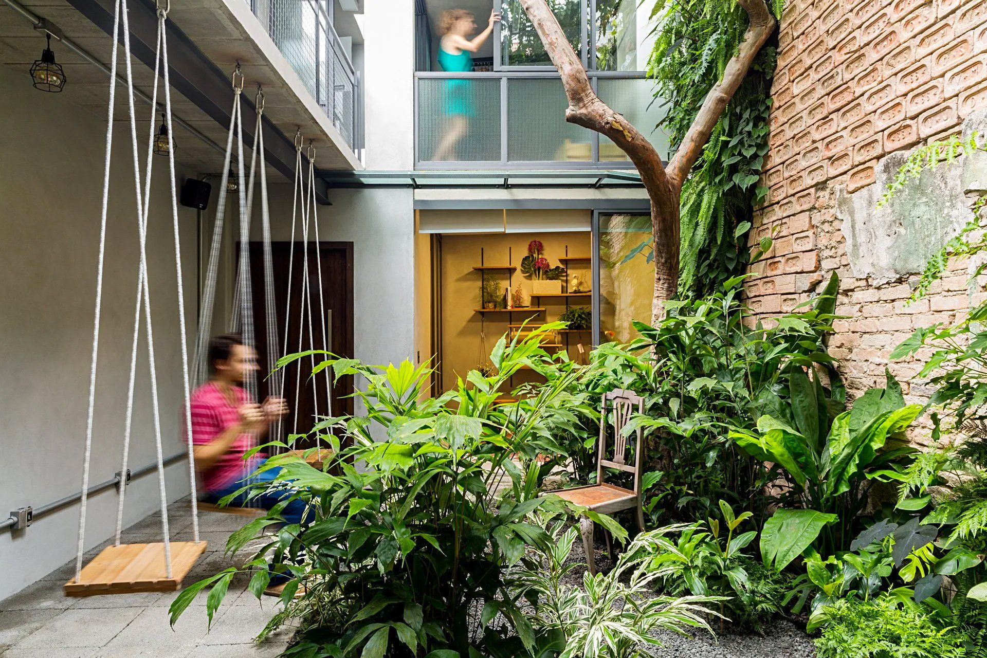 Um homem está sentado em um balanço em um pátio próximo a uma árvore.