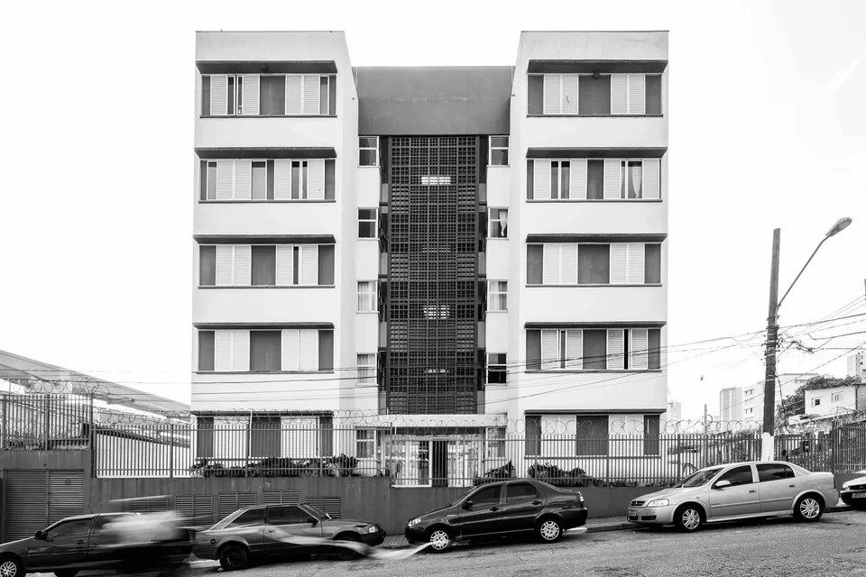 Uma foto em preto e branco de um prédio com carros estacionados em frente.