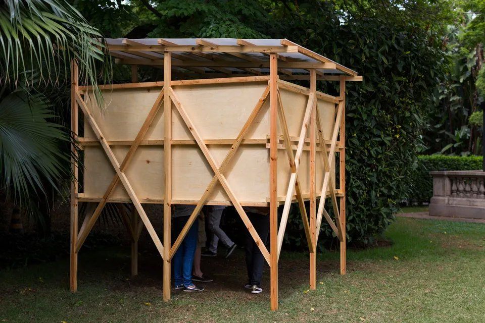 Um grupo de pessoas está sob uma estrutura de madeira em um parque.