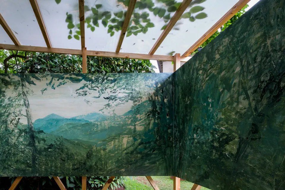 Uma grande pintura de uma paisagem está pendurada em uma estrutura de madeira.