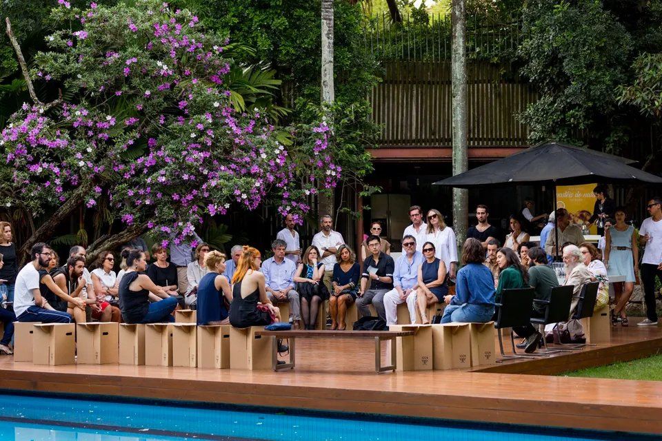 Um grupo de pessoas está sentado em bancos de madeira ao lado de uma piscina.
