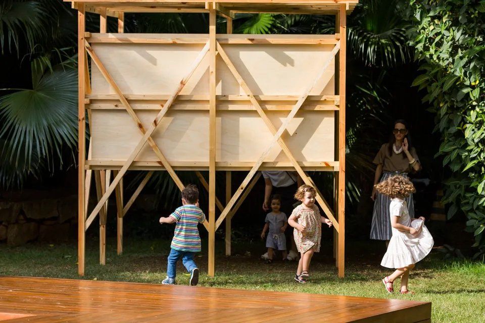 Um grupo de crianças brinca em frente a uma estrutura de madeira.