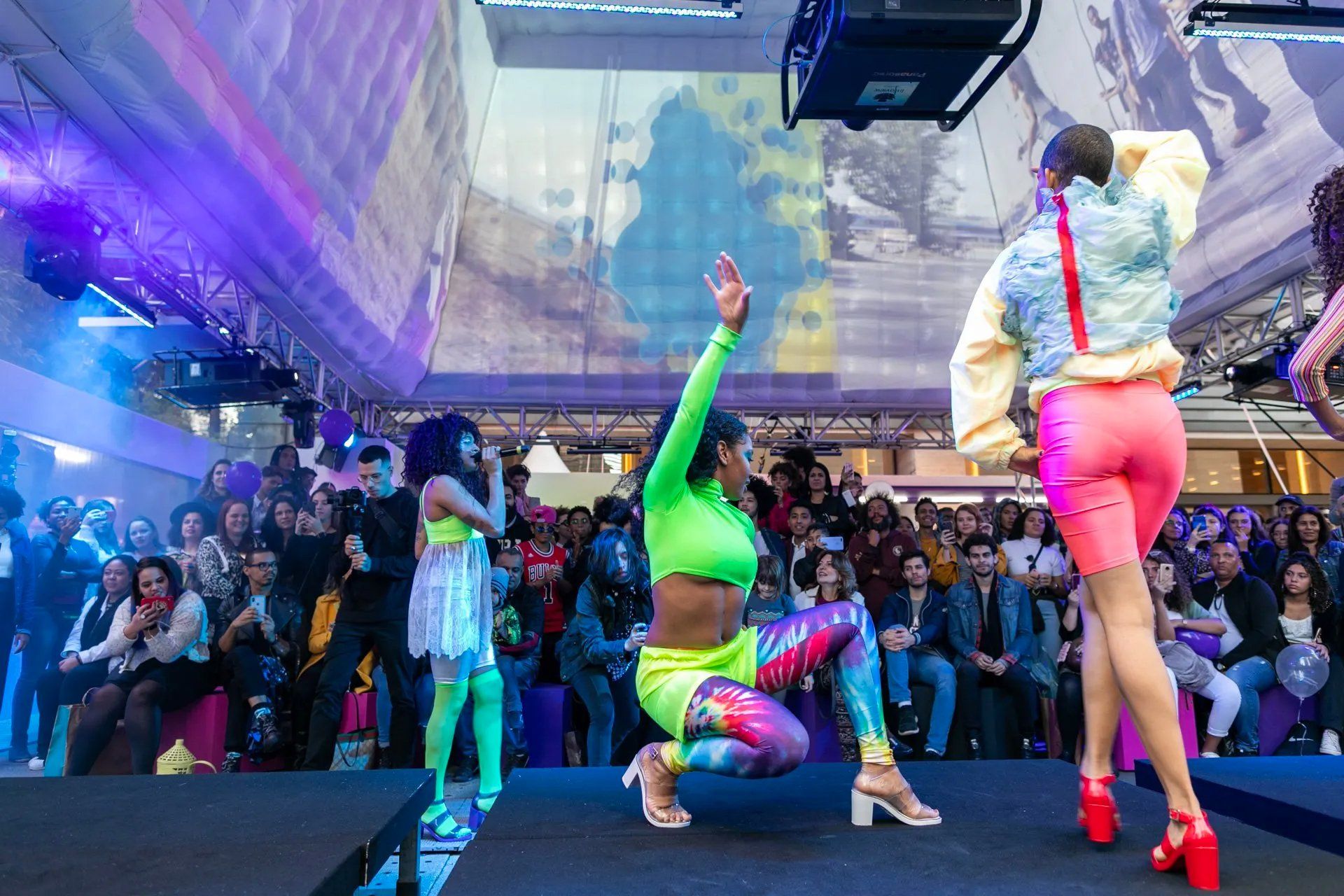 Um grupo de mulheres dança em um palco diante de uma multidão.