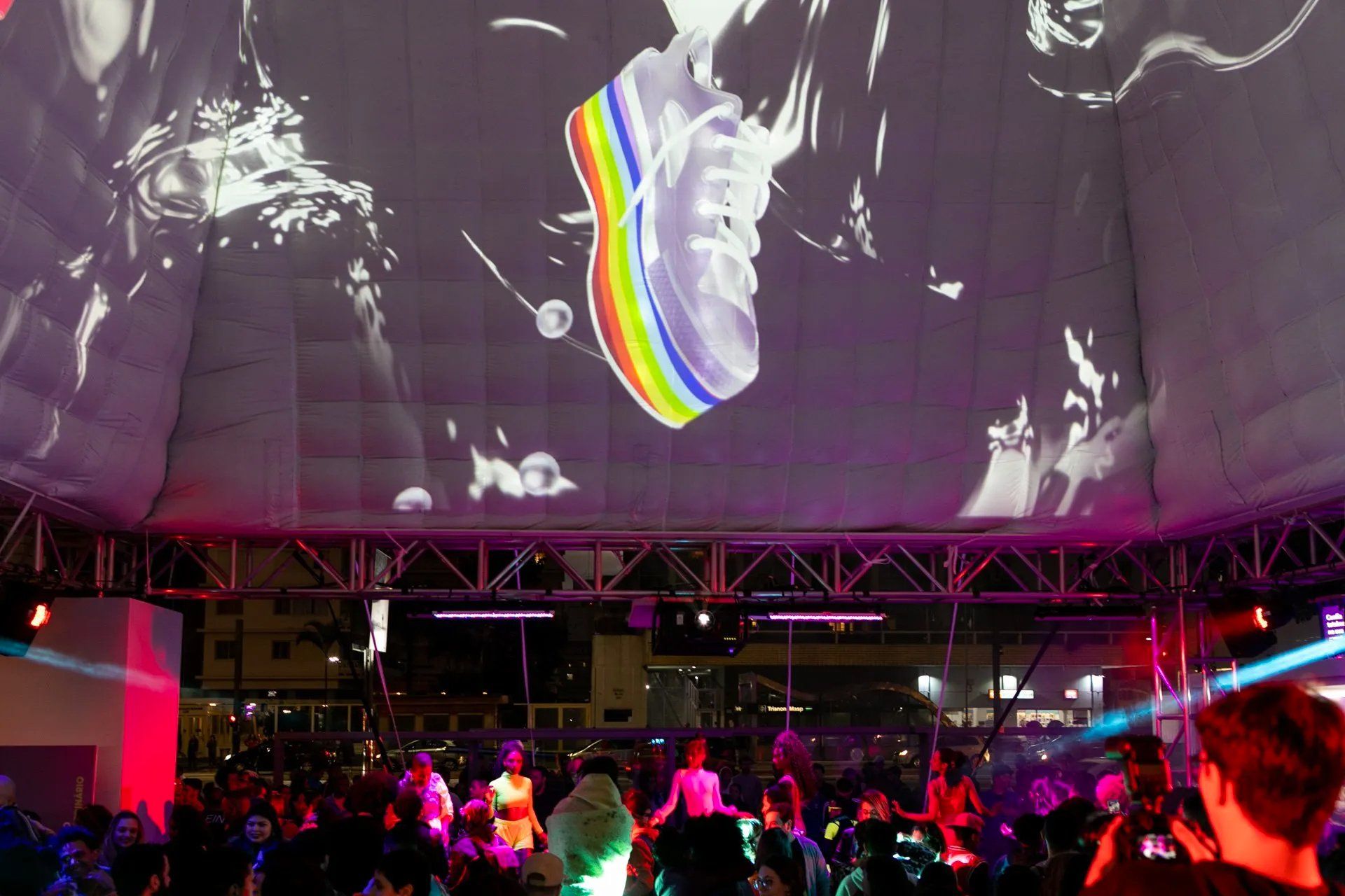Um sapato arco-íris é projetado no teto de uma sala lotada