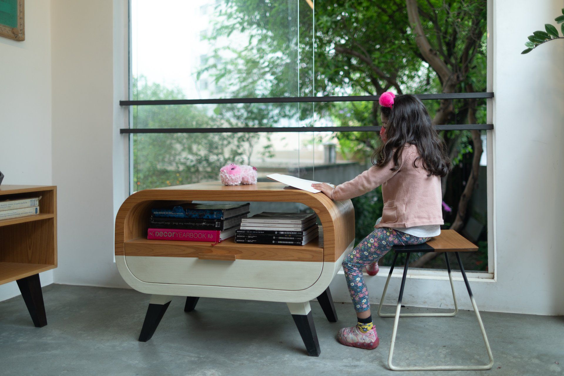 Uma menina está sentada à mesa lendo um livro.