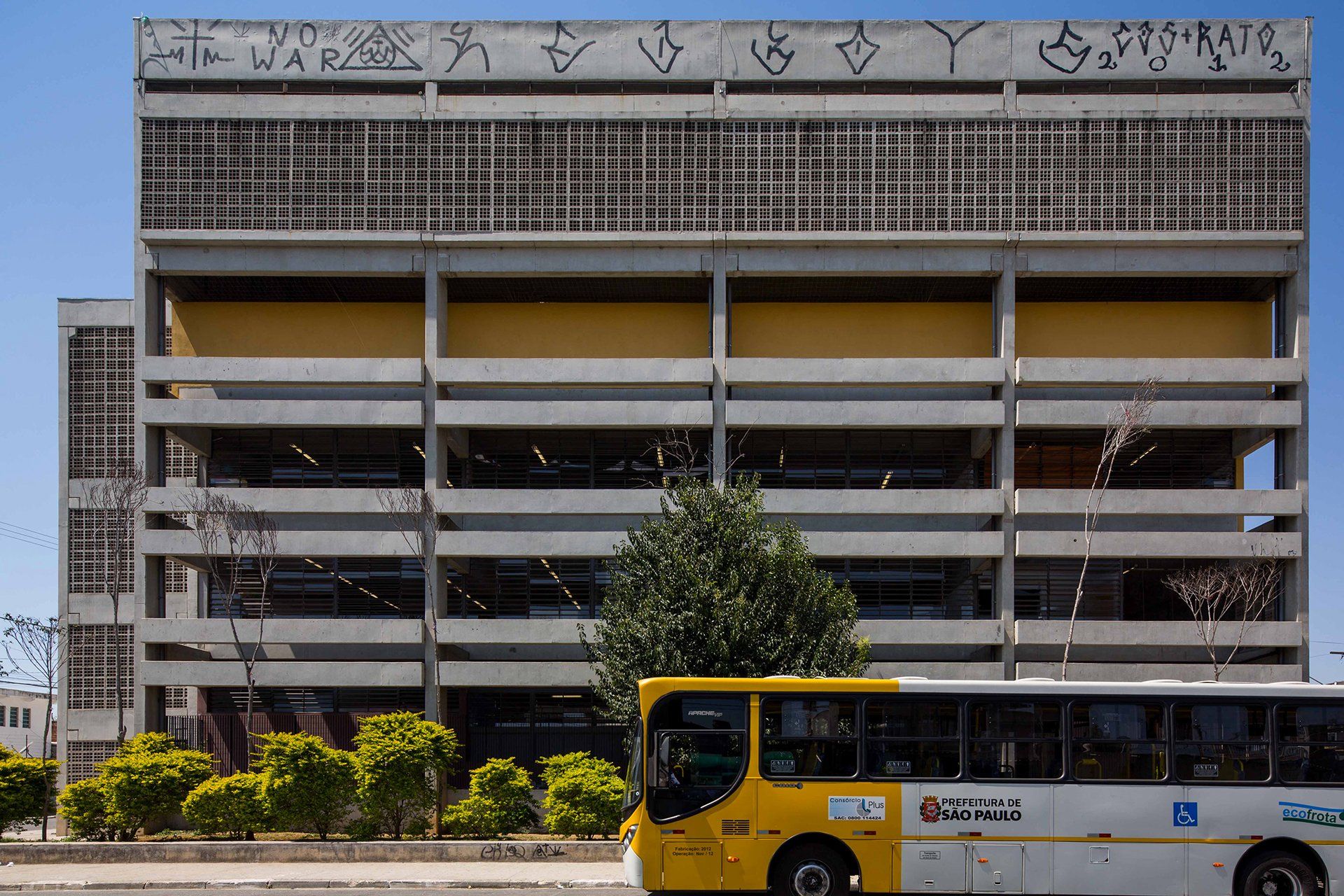 Um ônibus amarelo está estacionado em frente a um prédio com pichações