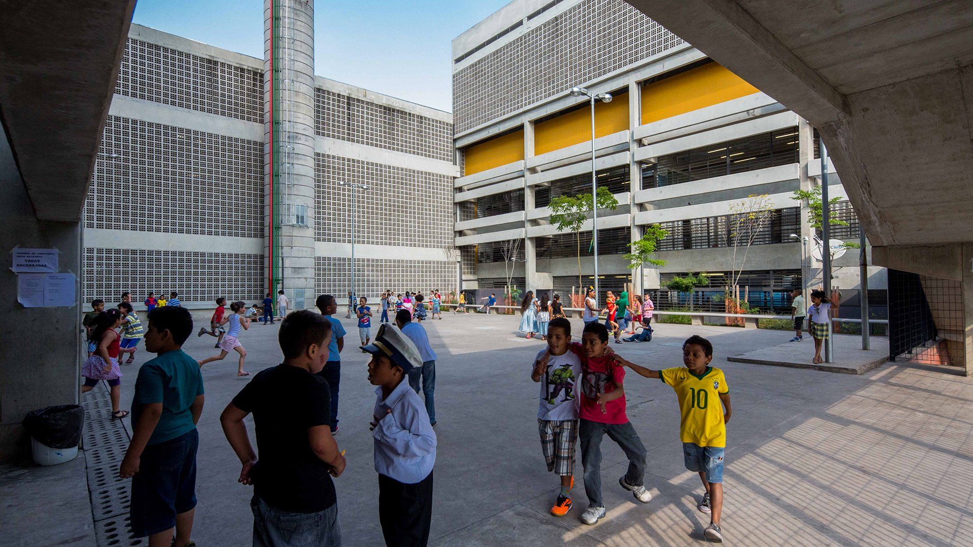 Um grupo de crianças brinca em um pátio em frente a um prédio.