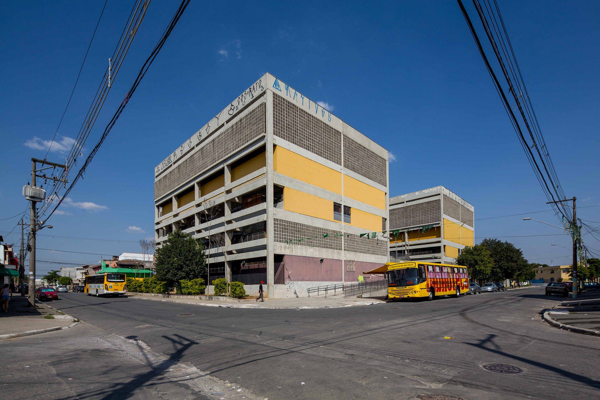 Um ônibus amarelo passa por uma rua em frente a um grande edifício.