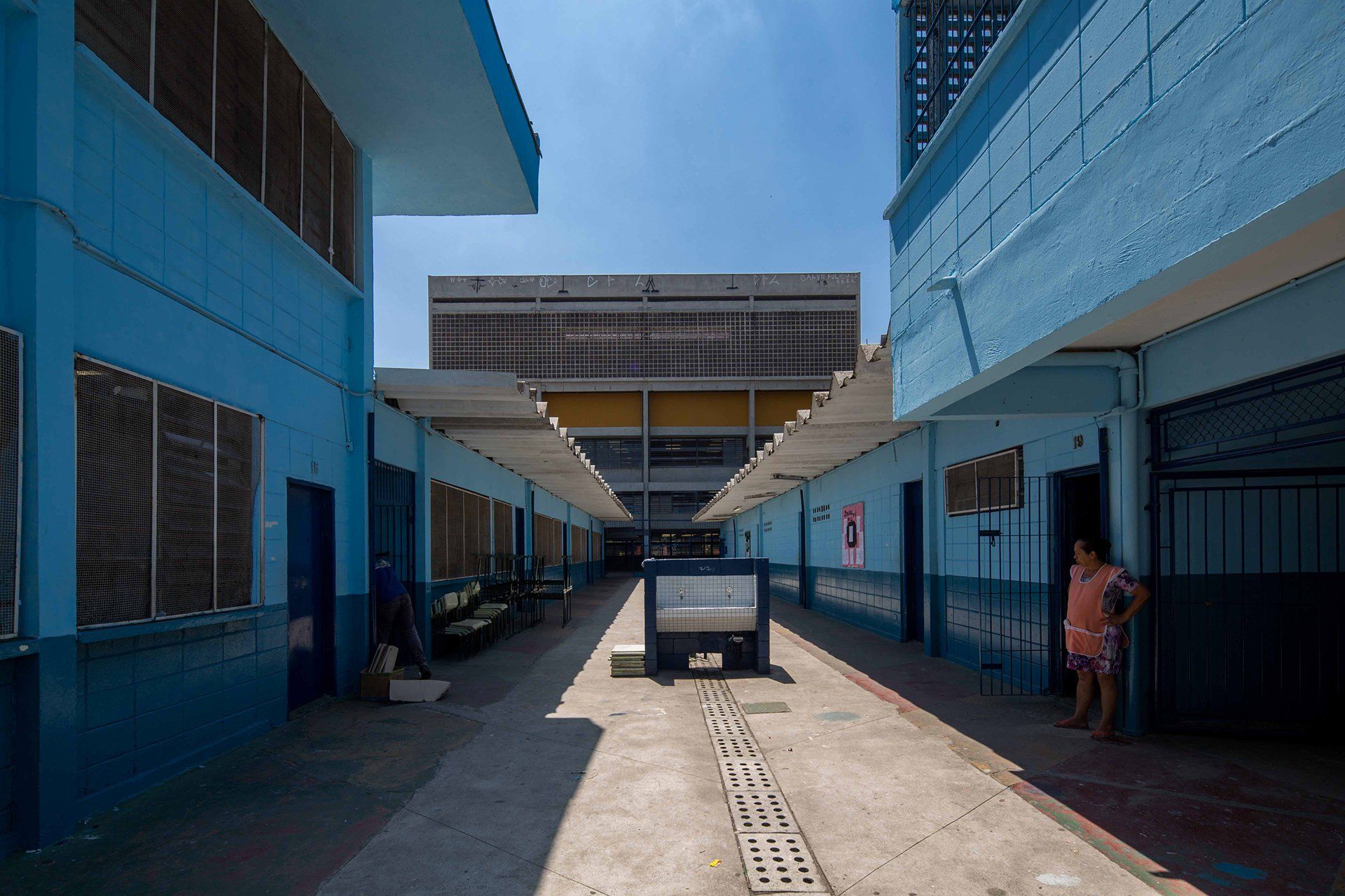 Uma mulher está parada em um corredor entre dois prédios azuis.
