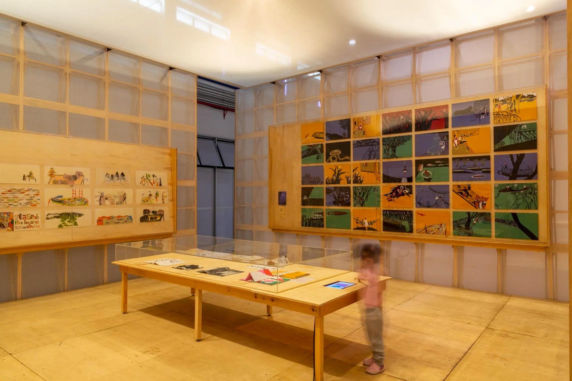 Uma garotinha está em uma sala com uma mesa e quadros na parede.