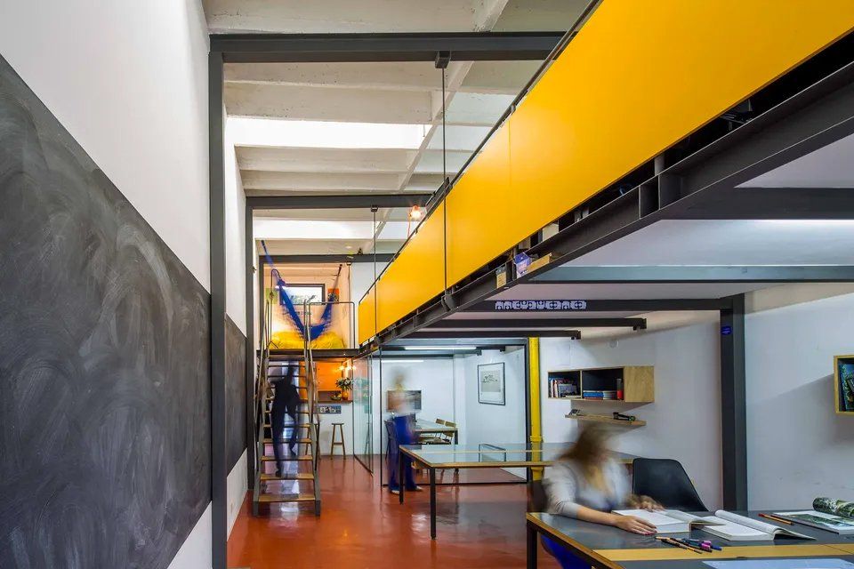 Uma mulher está sentada em uma mesa em uma sala com parede amarela.