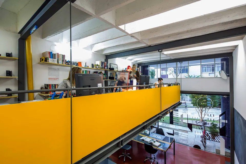 Um grupo de pessoas está sentado em mesas em um escritório com grade amarela.