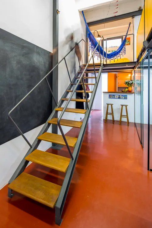 Uma escada de madeira que leva ao segundo andar com uma rede pendurada no teto.