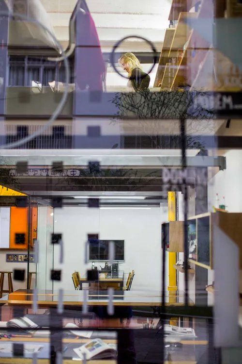 O reflexo de uma pessoa em um espelho em uma sala com mesa e cadeiras.