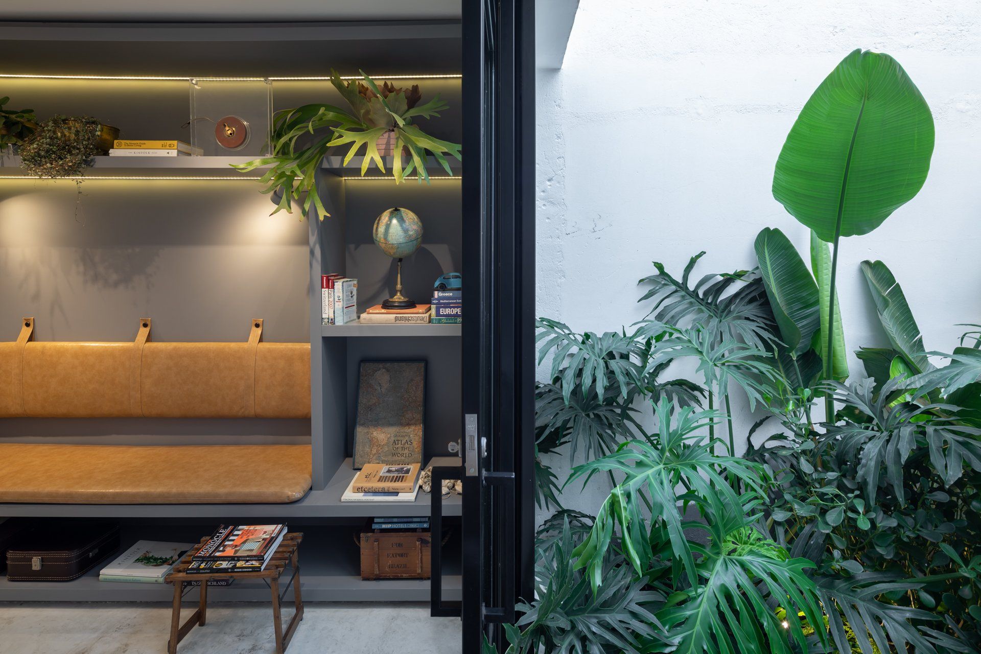 Uma sala com sofá, mesa, estantes e plantas.