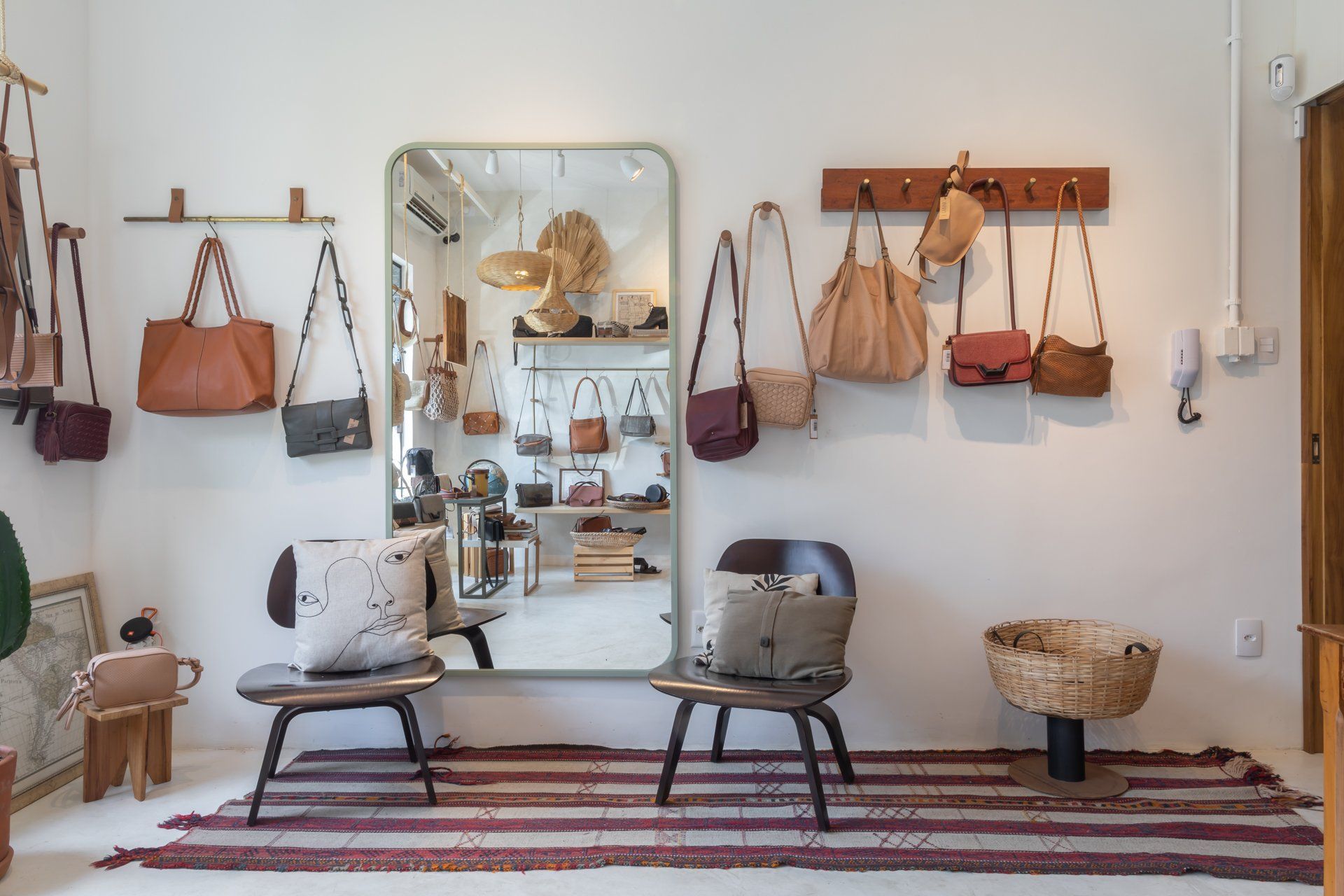 Uma sala com espelho, cadeiras, tapete e bolsas penduradas na parede.