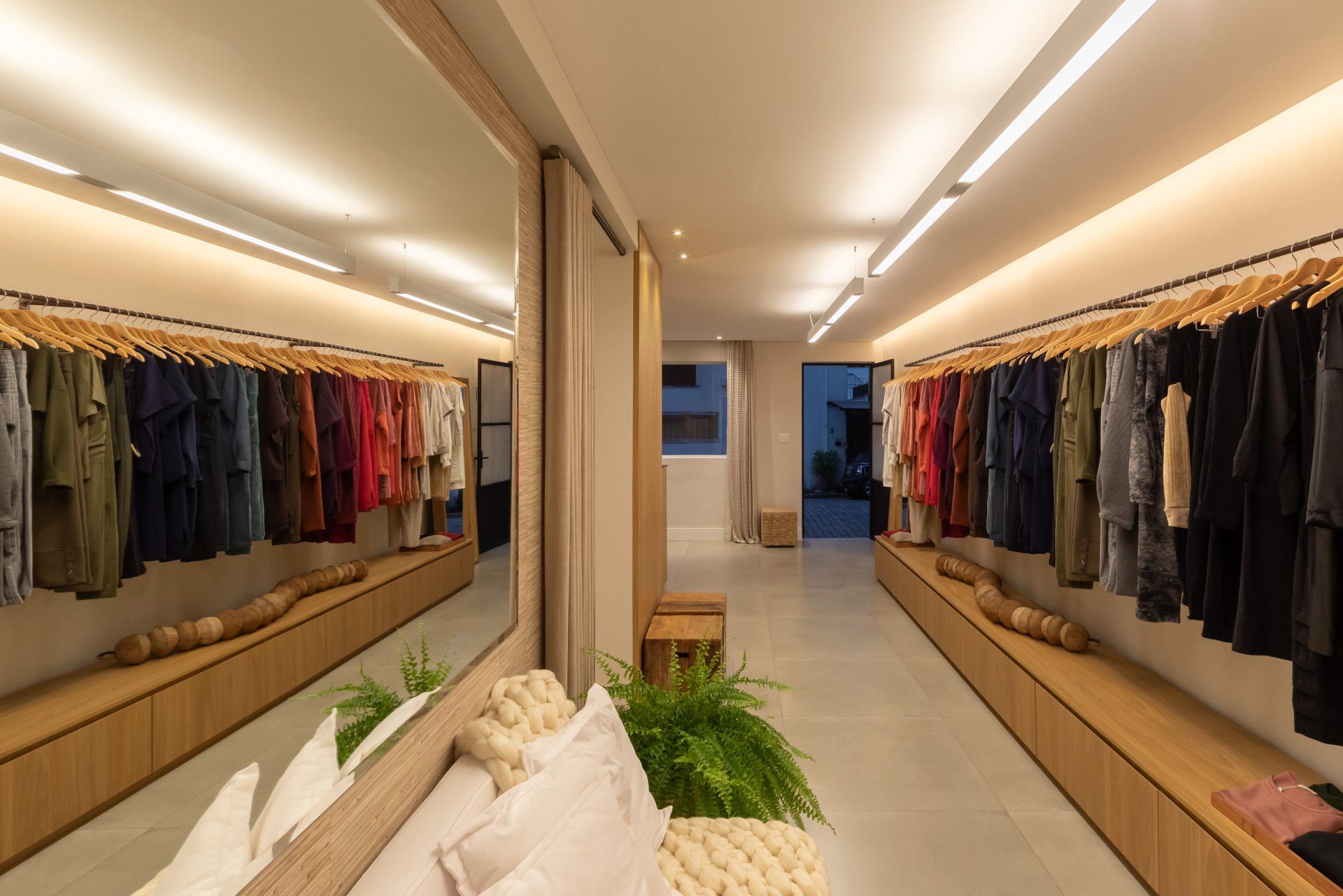 Um camarim com muitas roupas penduradas em cabides e um grande espelho.