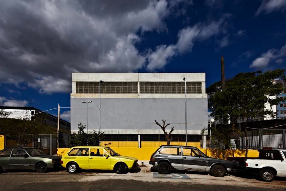 Uma fileira de carros está estacionada em frente a um prédio.