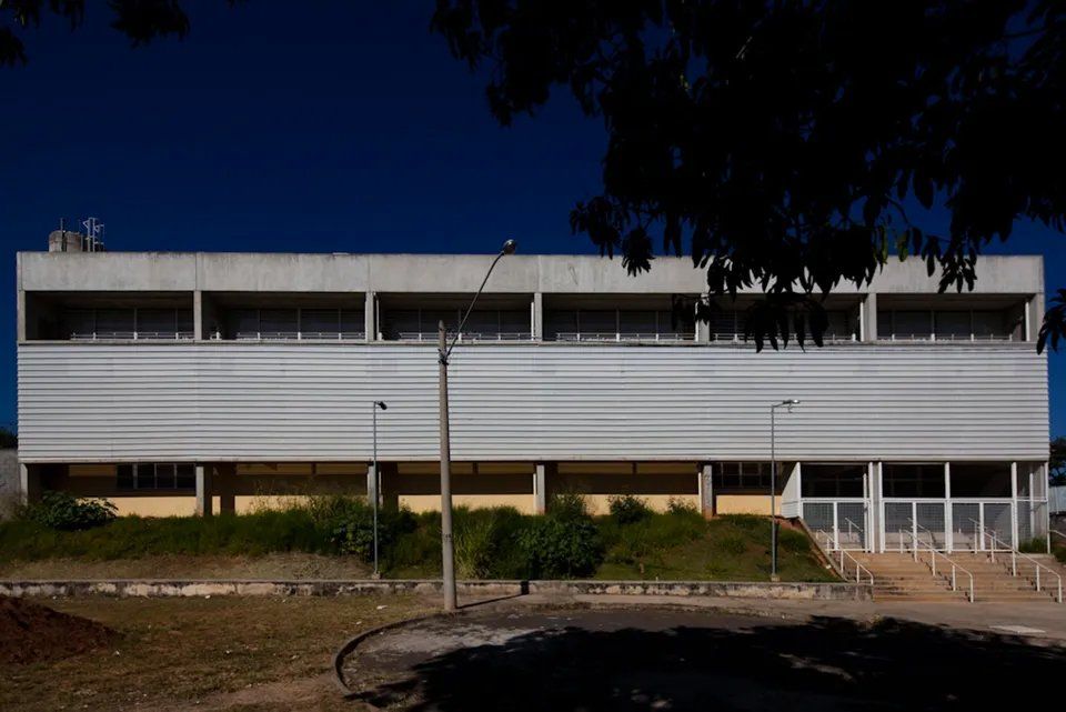 Um grande edifício com uma árvore na frente e um céu azul ao fundo.