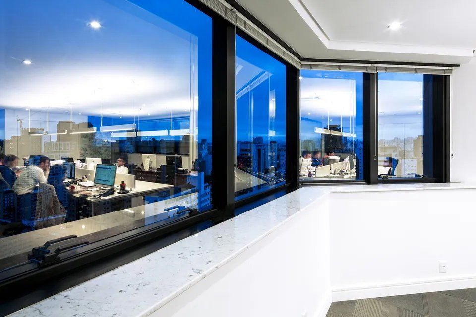 Uma sala com muitas janelas e pessoas sentadas em mesas