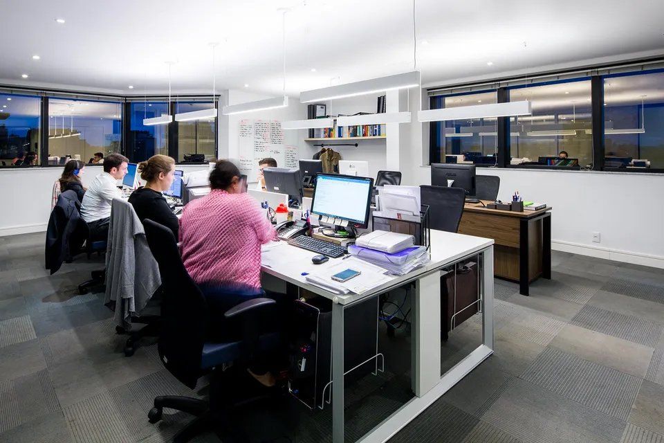 Um grupo de pessoas está sentado em mesas de um escritório trabalhando em computadores.