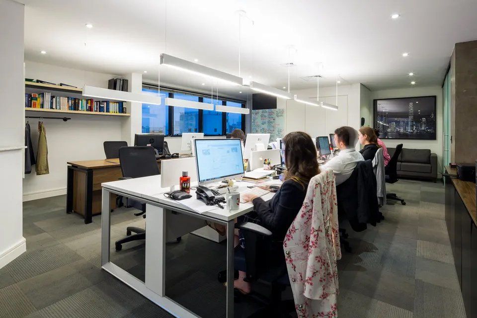 Um grupo de pessoas está sentado em mesas de um escritório trabalhando em computadores.