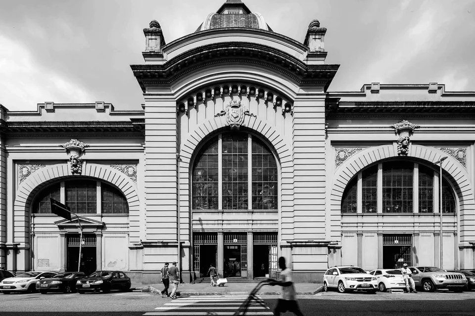 Uma foto em preto e branco de um grande prédio com carros estacionados em frente.