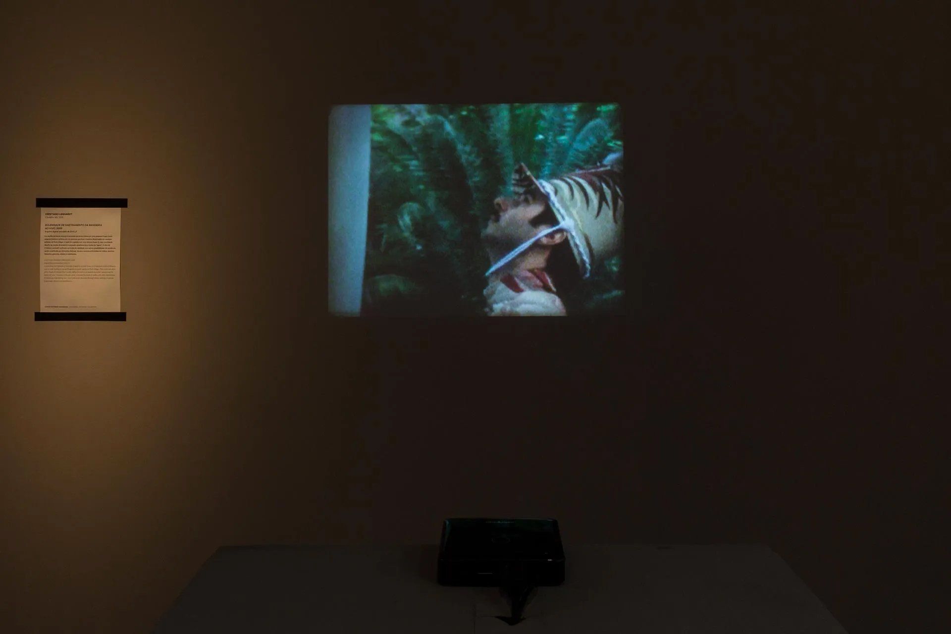 Um homem de chapéu está em uma tela em um quarto escuro.