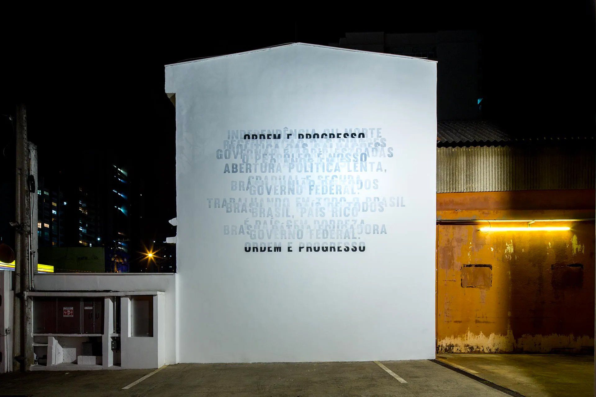 Uma grande parede branca com grafites fica em frente a um prédio à noite.