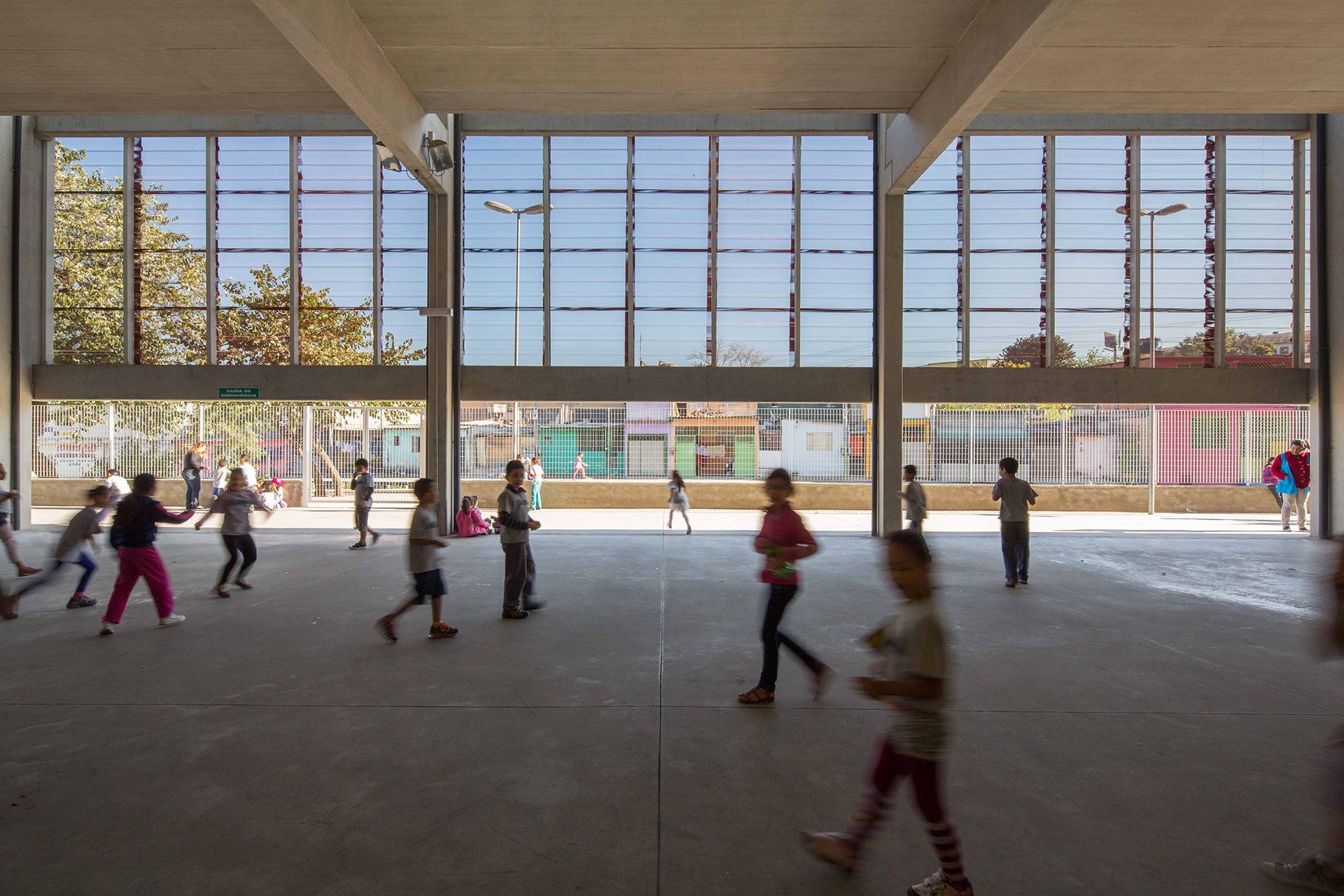 Um grupo de crianças brinca em uma sala grande com muitas janelas.