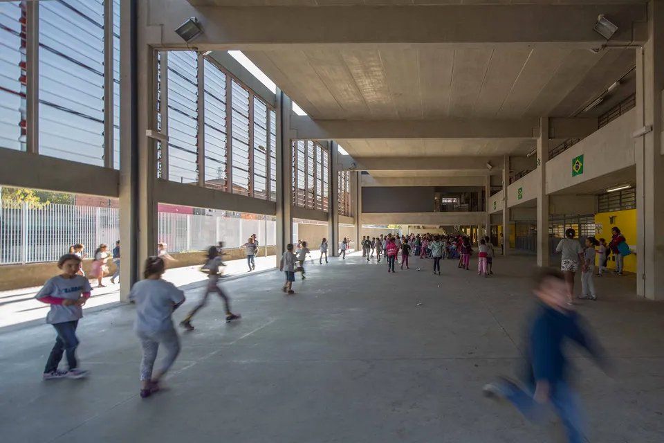 Um grupo de crianças está brincando em uma grande sala de uma escola.