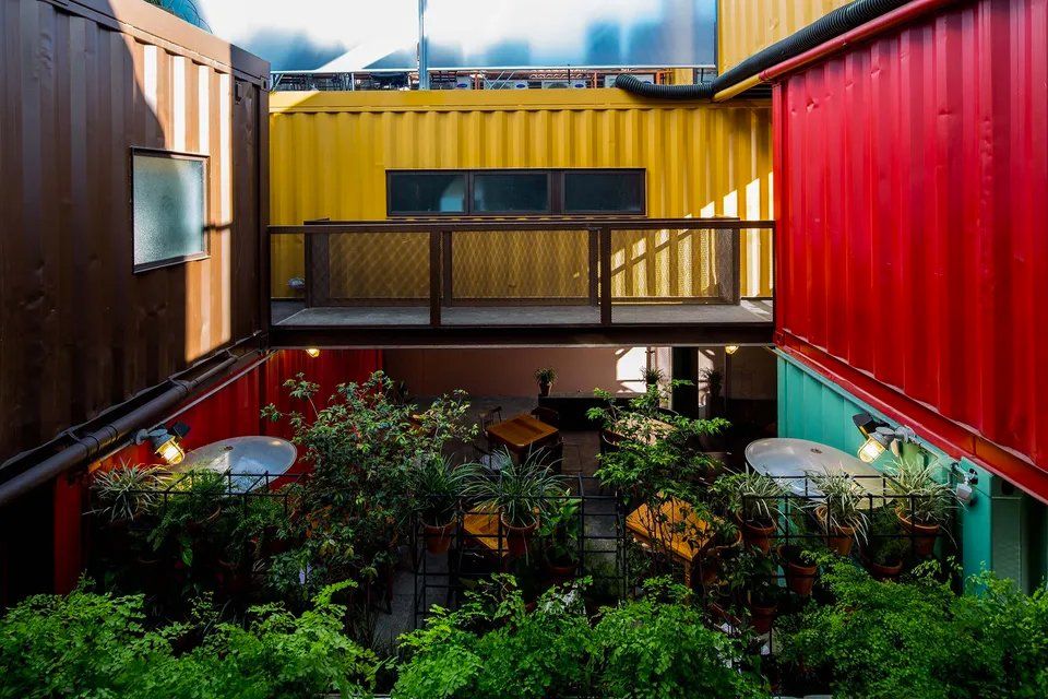 Um pátio cheio de mesas e cadeiras entre dois contêineres.