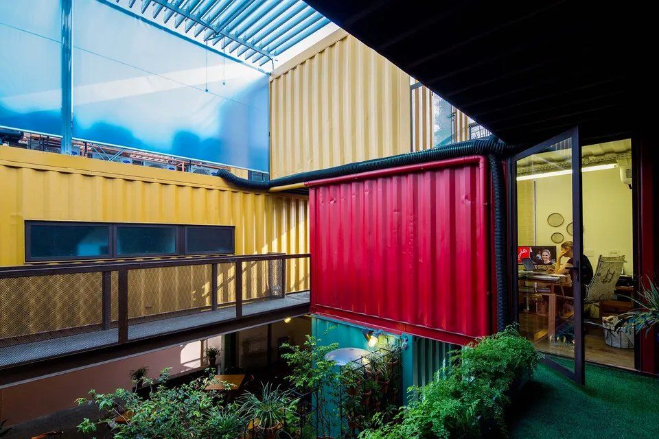 Um homem está sentado a uma mesa em uma sala entre dois prédios.