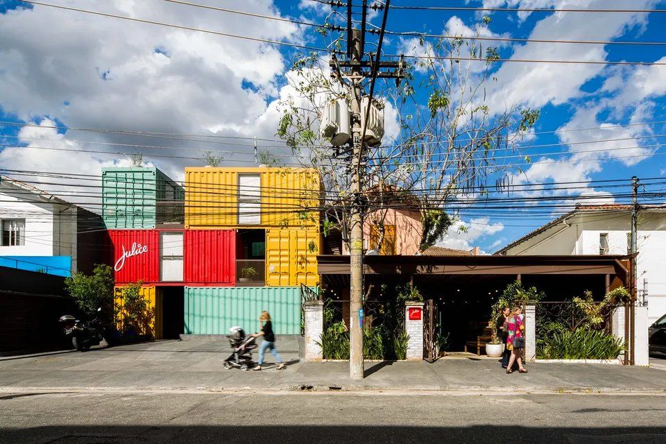 Um grupo de pessoas caminha por uma rua em frente a um prédio feito de contêineres.