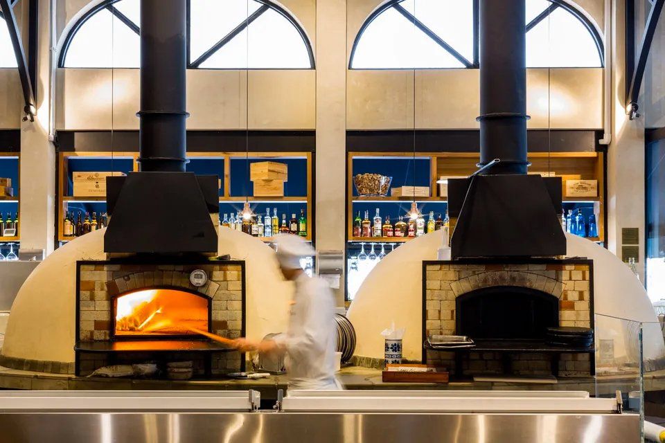 Um homem está diante de dois fornos de pizza em um restaurante.