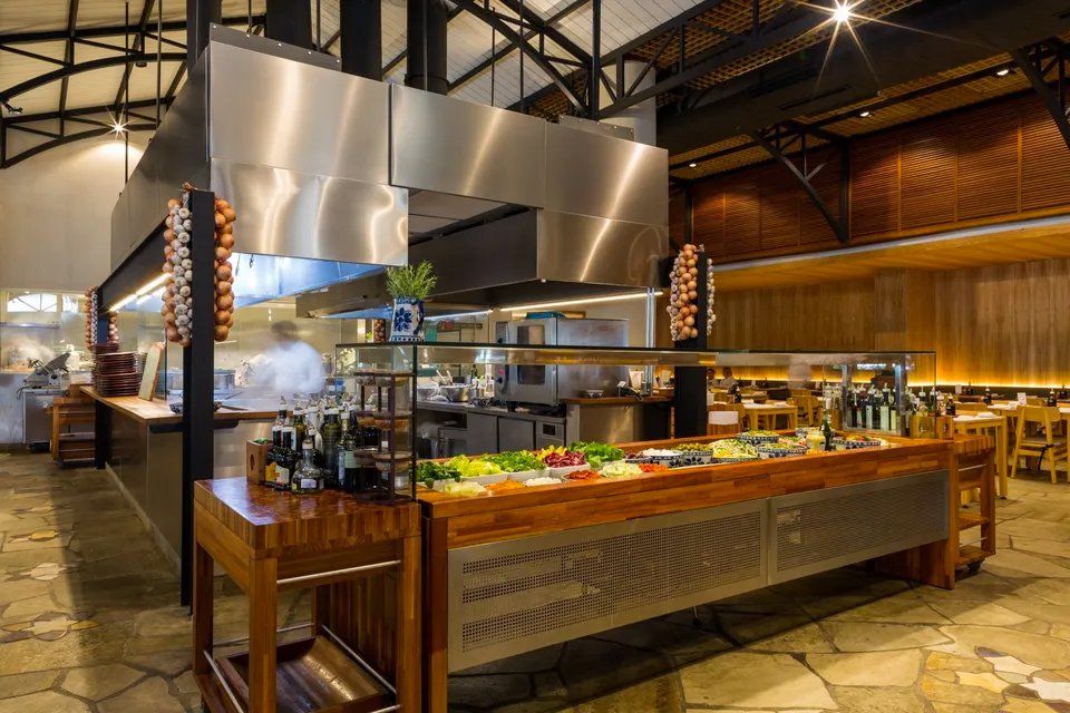 Uma grande cozinha com eletrodomésticos de aço inoxidável e mesas de madeira.